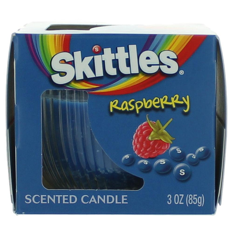 Skittles Raspberry scented candle in a 3 oz jar with colorful Skittles branding and a lit wick on a wooden surface.